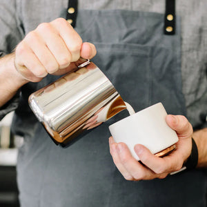 Barista versa latte da una lattiera in acciaio inox lucido, parte degli accessori per Espresso e lattiera, tutto sul caffè.