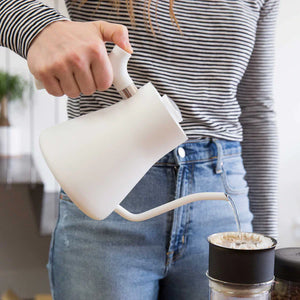 Mano che versa acqua da un bollitore bianco con beccuccio stretto nel filtro del caffè, parte di EspressoGear, tutto sul caffè.